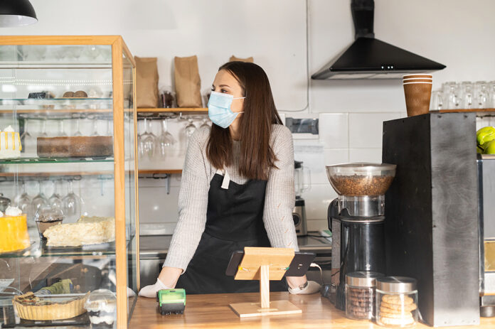 A Female Bakery Owner Wearing Mask And Gloves Stands Behind The