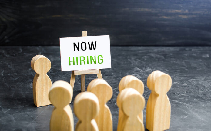 A Man With A Now Hiring Sign Appeals To The Crowd About Hiring.
