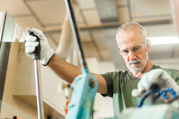 Older Worker Threading A Steel Bar In An Industrial Factory