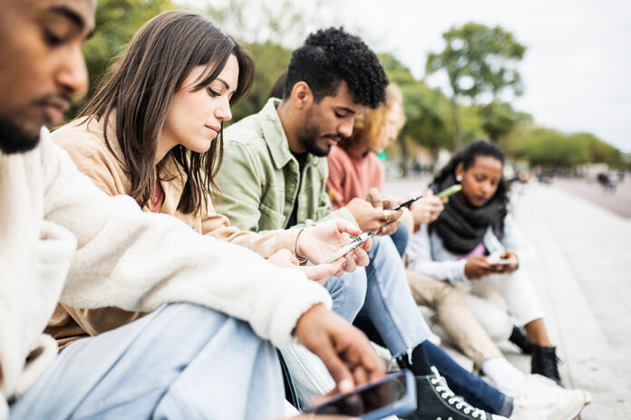 Group Of Young Adult Friends Using Smartphones Outdoors - Addict