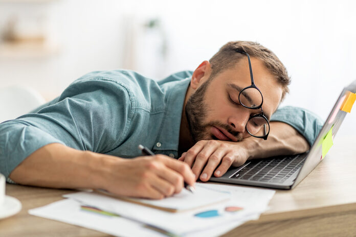 Exhausted Millennial Man Sleeping On His Office Desk, Next To La