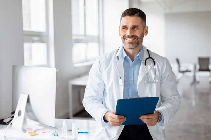 Portrait Of Middle Aged Male Doctor Holding Clipboard, Looking A