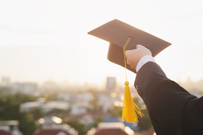 Happy Young Asian Graduate Student In Graduation Gown And Cap In