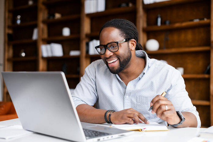 Smiling African-american Guy Takes Notes Watching Webinars On Th
