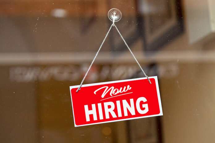 Red Sign Hanging At The Glass Door Of A Shop Saying: "now Hiring