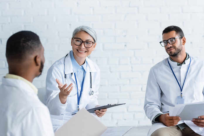 Smiling Asian Doctor Pointing At Blurred African Colleague Durin