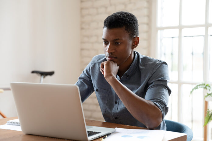 Serious African Worker Sitting At Desk Reading Email Feels Conce