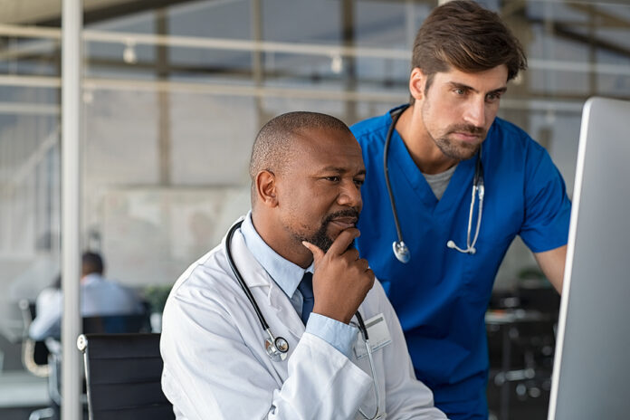Mature african doctor and nurse analyze medical report on comput